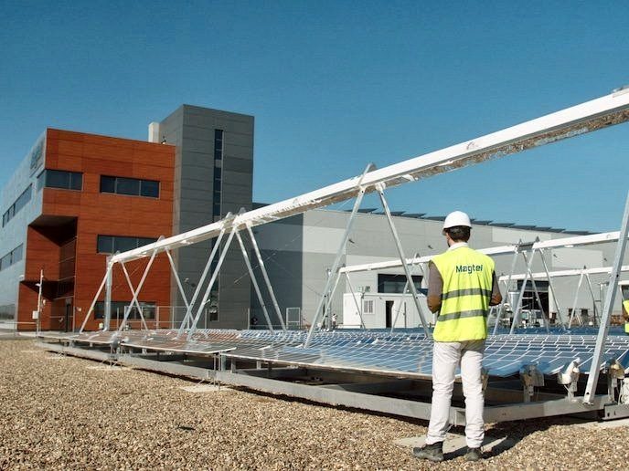 A technician in a vest in front of the collector, with the mirrors installed and a building with an orange façade in the background