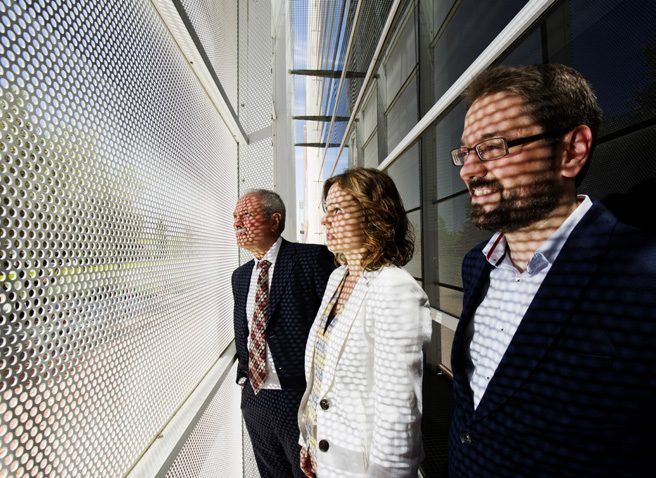 Three team members look through a perforated metal façade