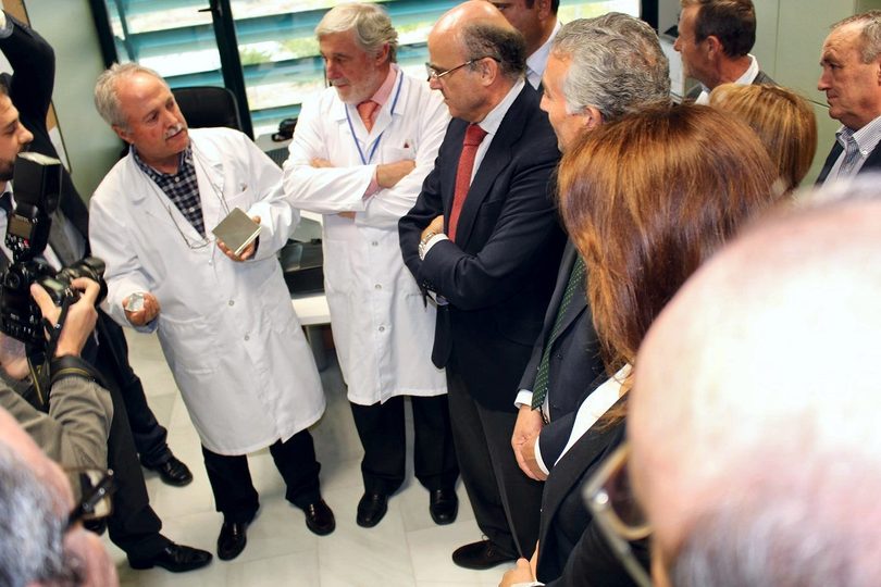 Two technicians in white coats explain the project to Minister Luis de Guindos
