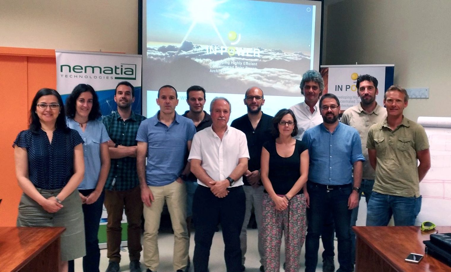 About twenty people pose in a meeting room with the IN-POWER and Nematia roll-ups