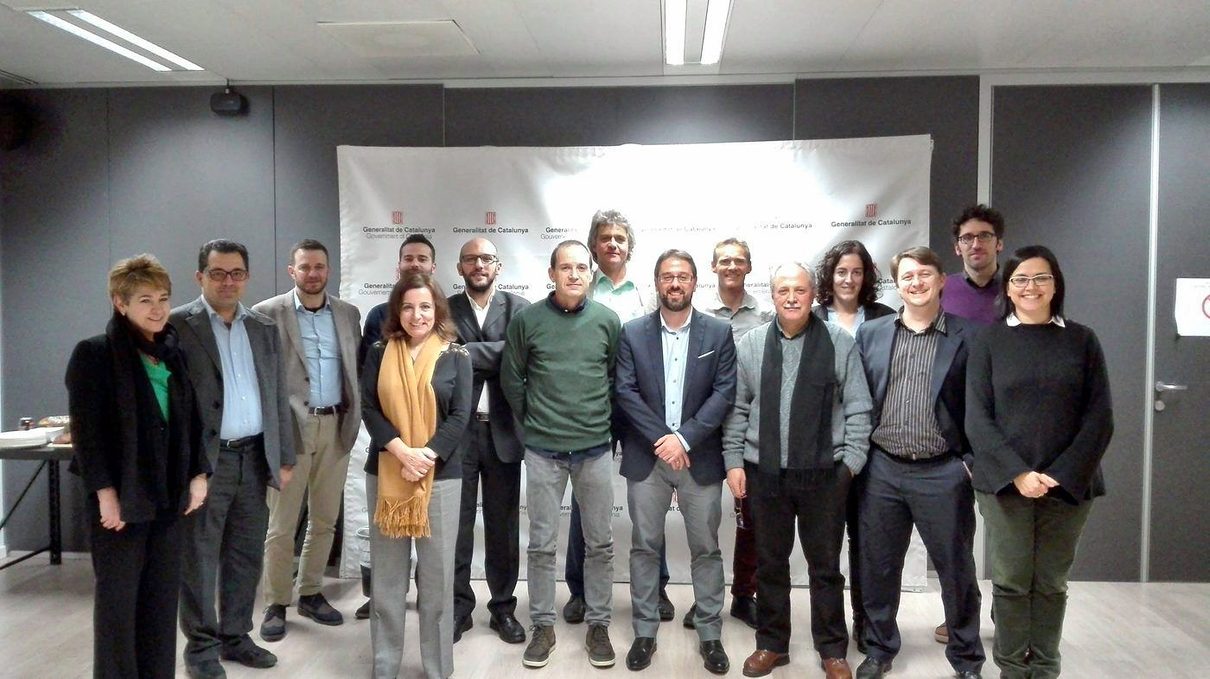 About twenty consortium members pose in a room in front of a white panel