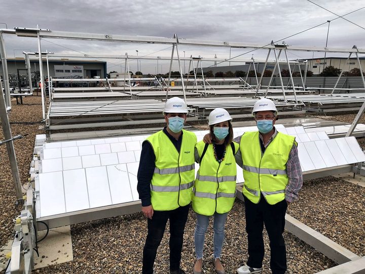 Three people in high-visibility vests and face masks pose in front of the rows of mirrors at the plant