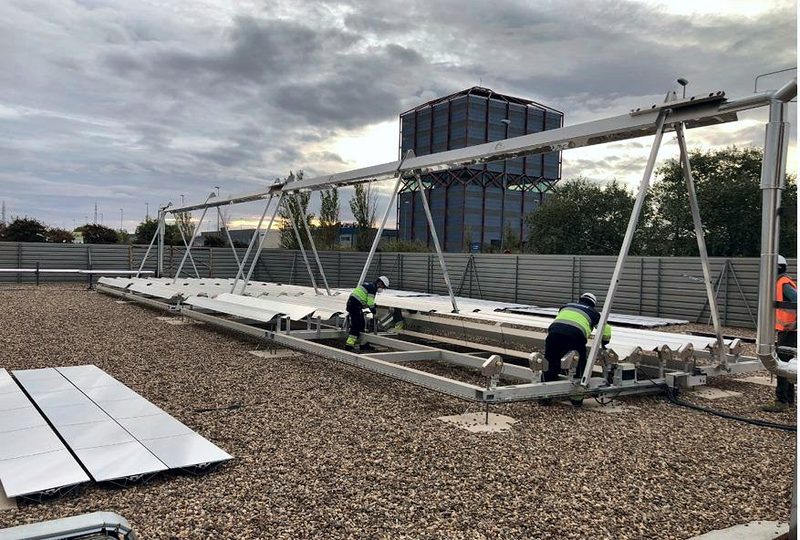 Workers mount the rows of mirrors under the collector structure, on a gravel roof