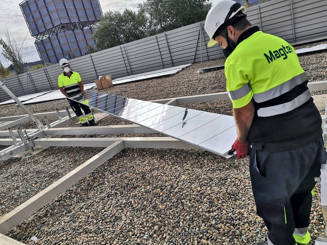 A worker in a hard hat places a row of mirrors on the structure while another works in the background