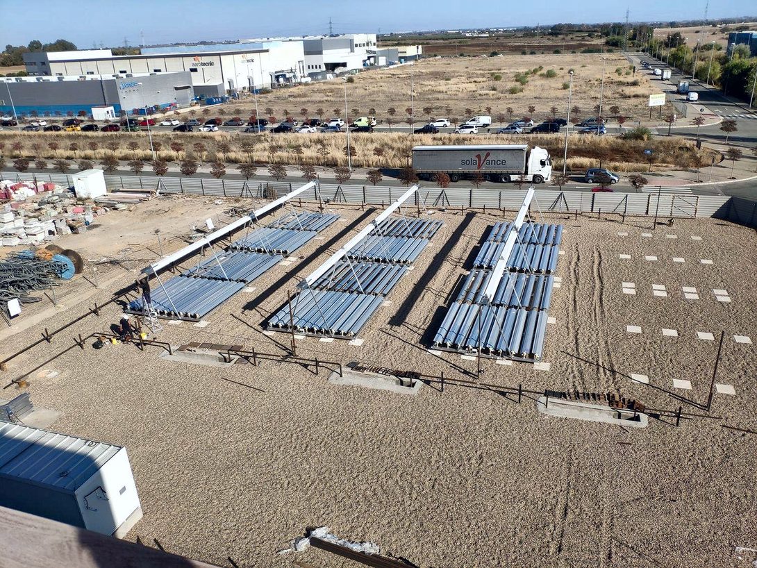 Aerial view of a plot with rows of solar collectors under construction next to an industrial estate
