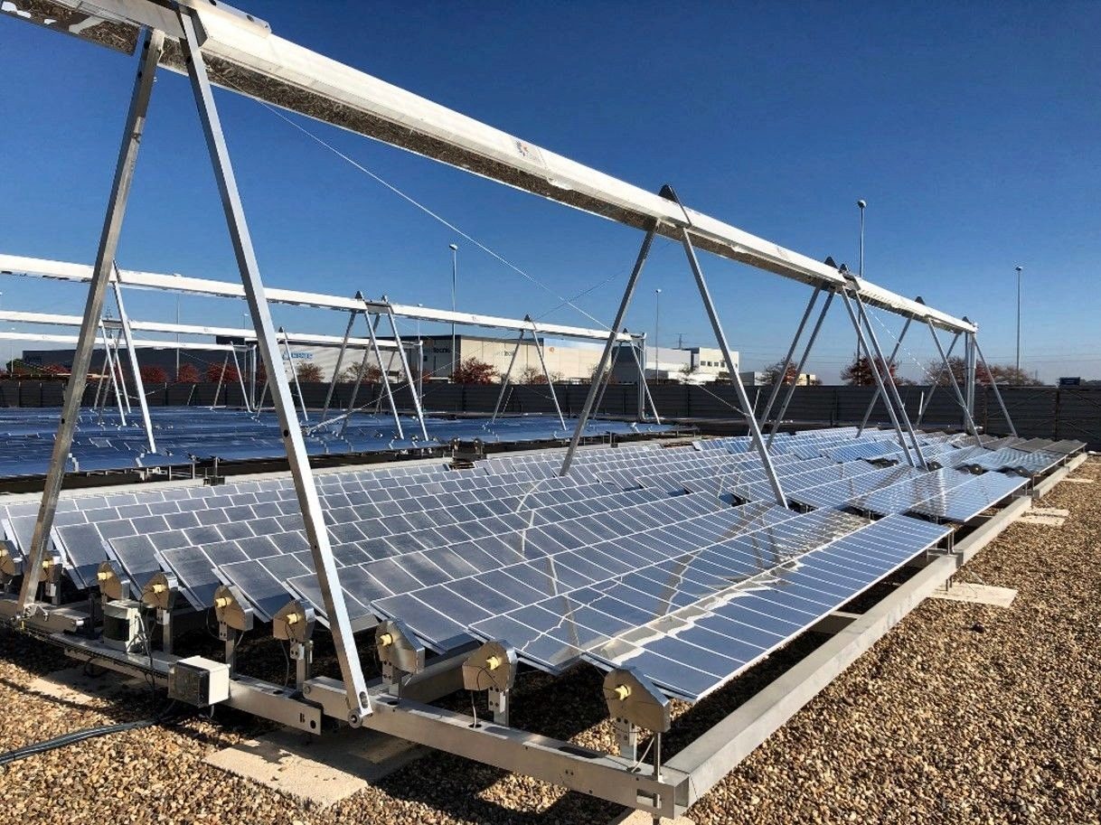 Rows of rectangular mirrors mounted on the metal structure of a Fresnel collector, under a blue sky