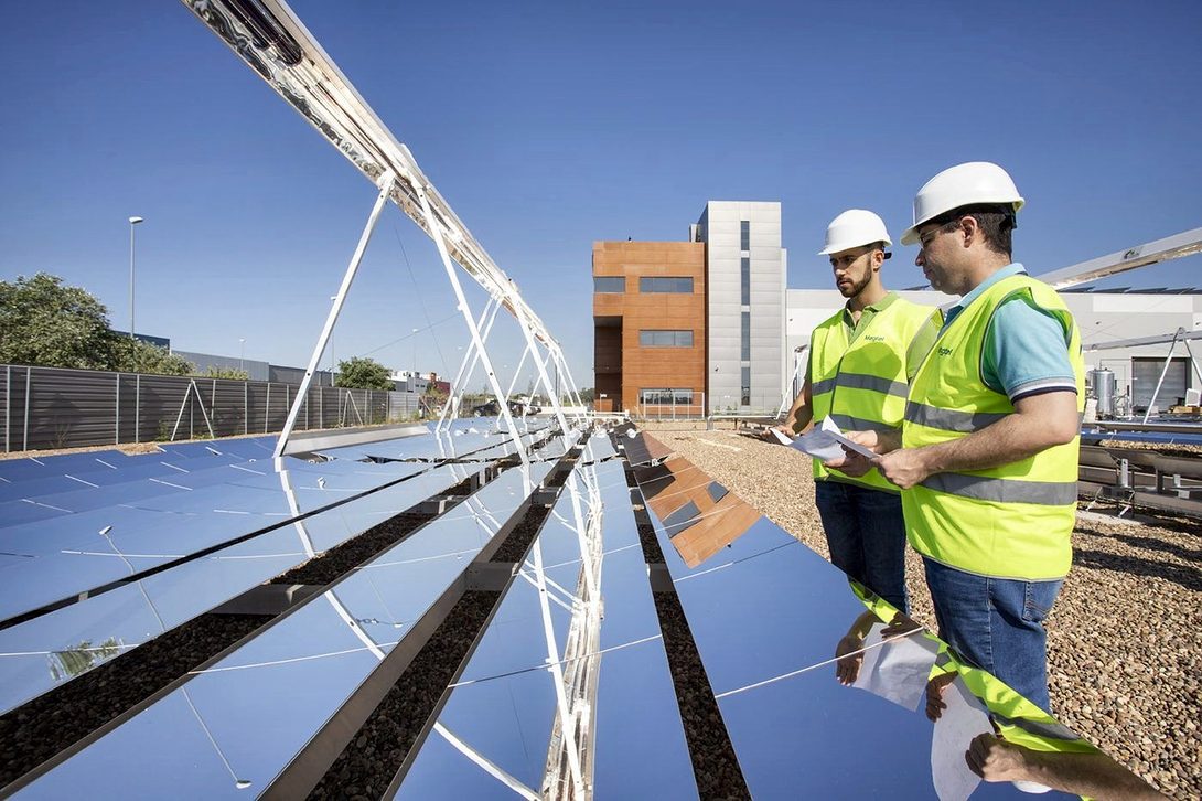 Two technicians in hard hats and vests look over some drawings next to a solar collector
