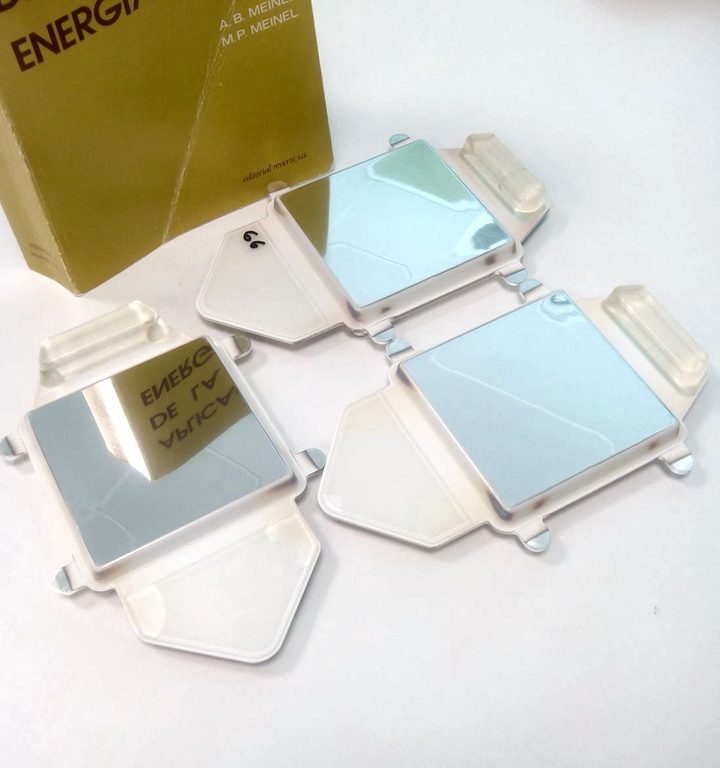 REFLEXIS samples of 10 by 10 centimetres on a table, next to the book Aplicaciones de la energía solar