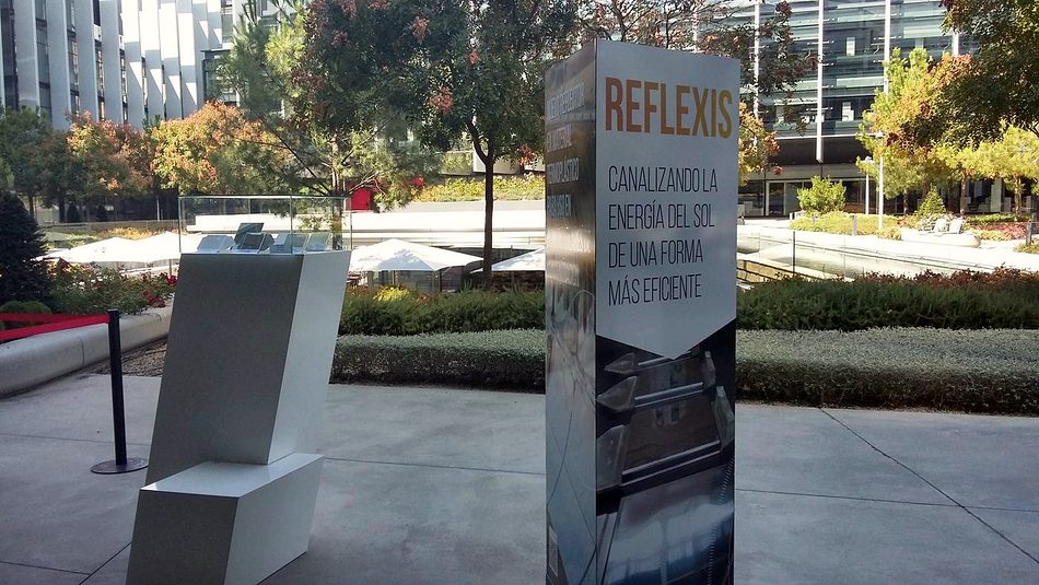 A display totem with the REFLEXIS sign next to a pedestal with a prototype, in a corporate garden