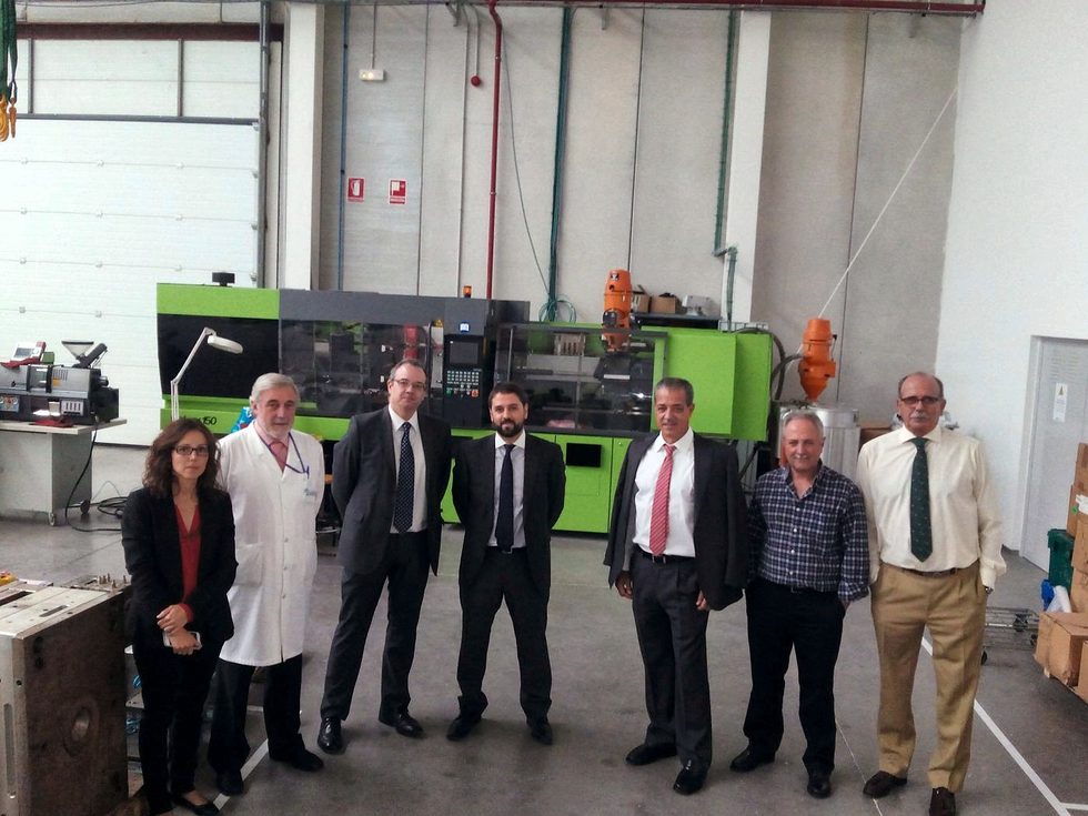 Group of people in an industrial building with injection moulding machines, two of them in white coats
