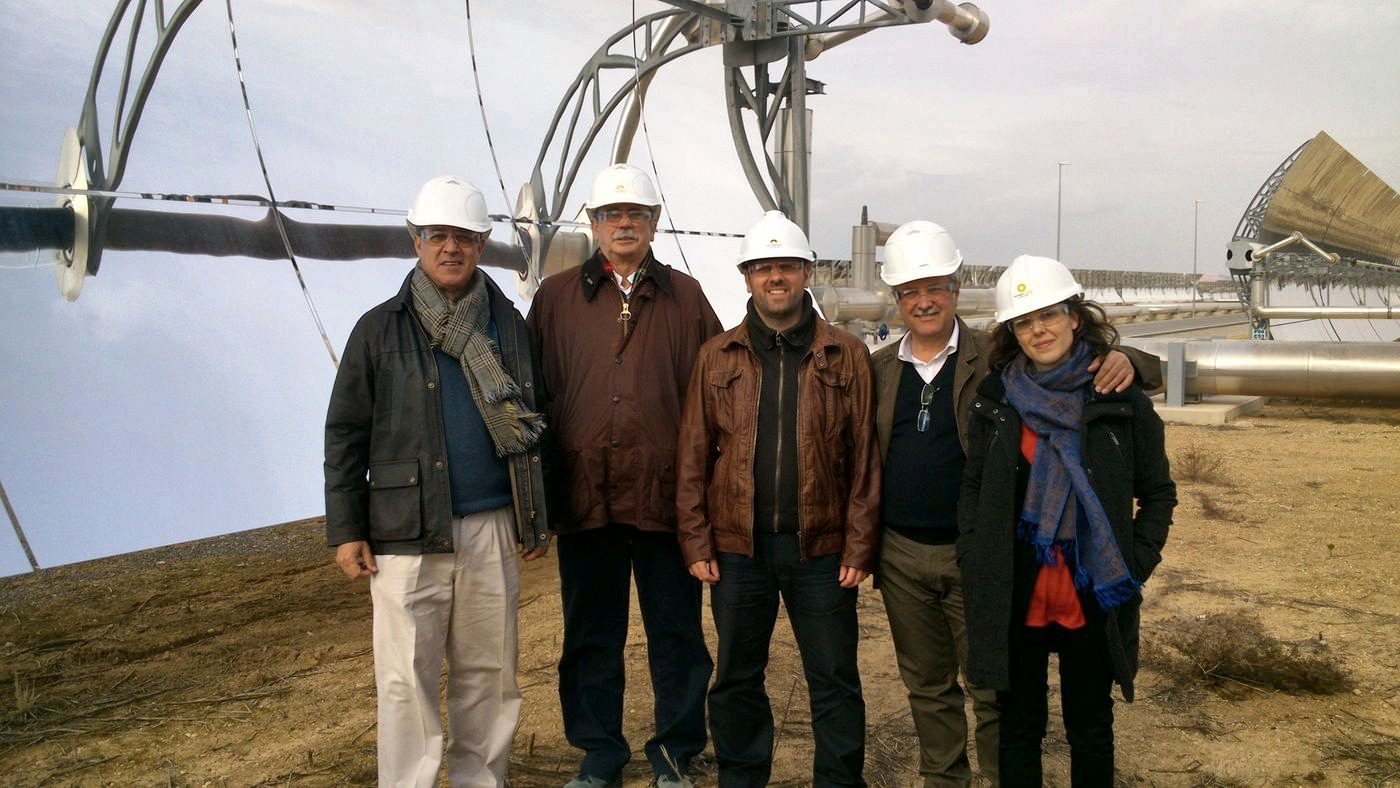 Six people in hard hats pose in front of the parabolic trough collectors of a solar thermal power plant