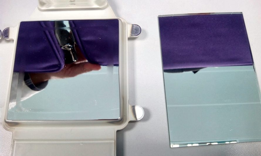 REFLEXIS mirror sample in its plastic frame, on the left, next to a glass mirror; both reflect the same purple cloth